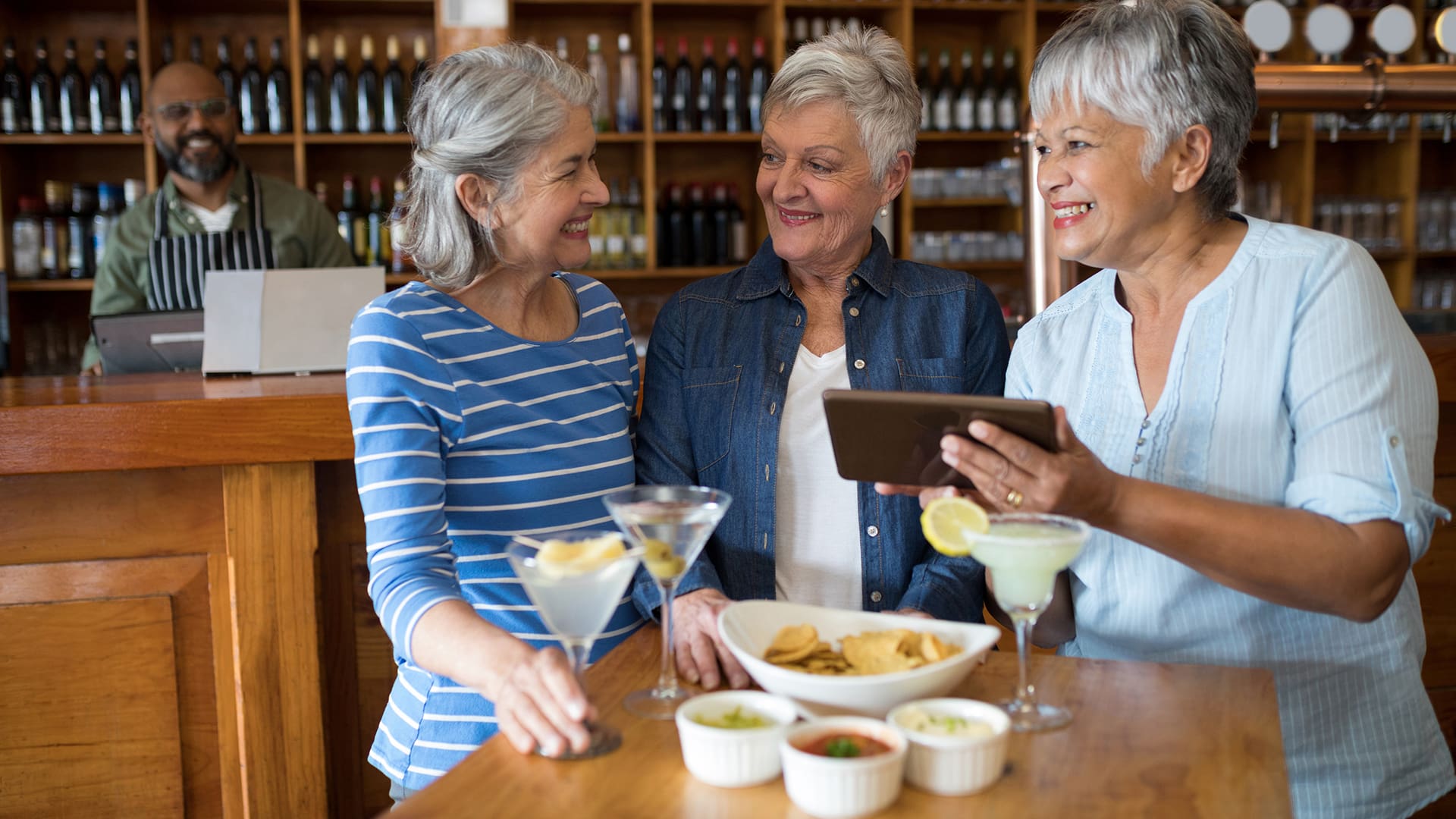 Senior female friends using digital tablet while having drinks in bar