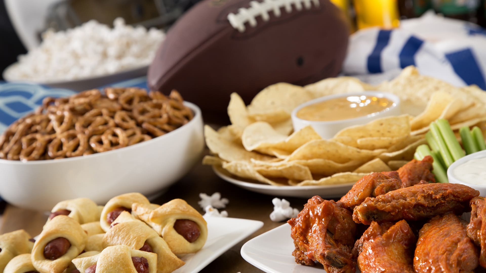 Hot wings, nachos, pigs in a blanket, beer, and popcorn, a tailgate party spread.