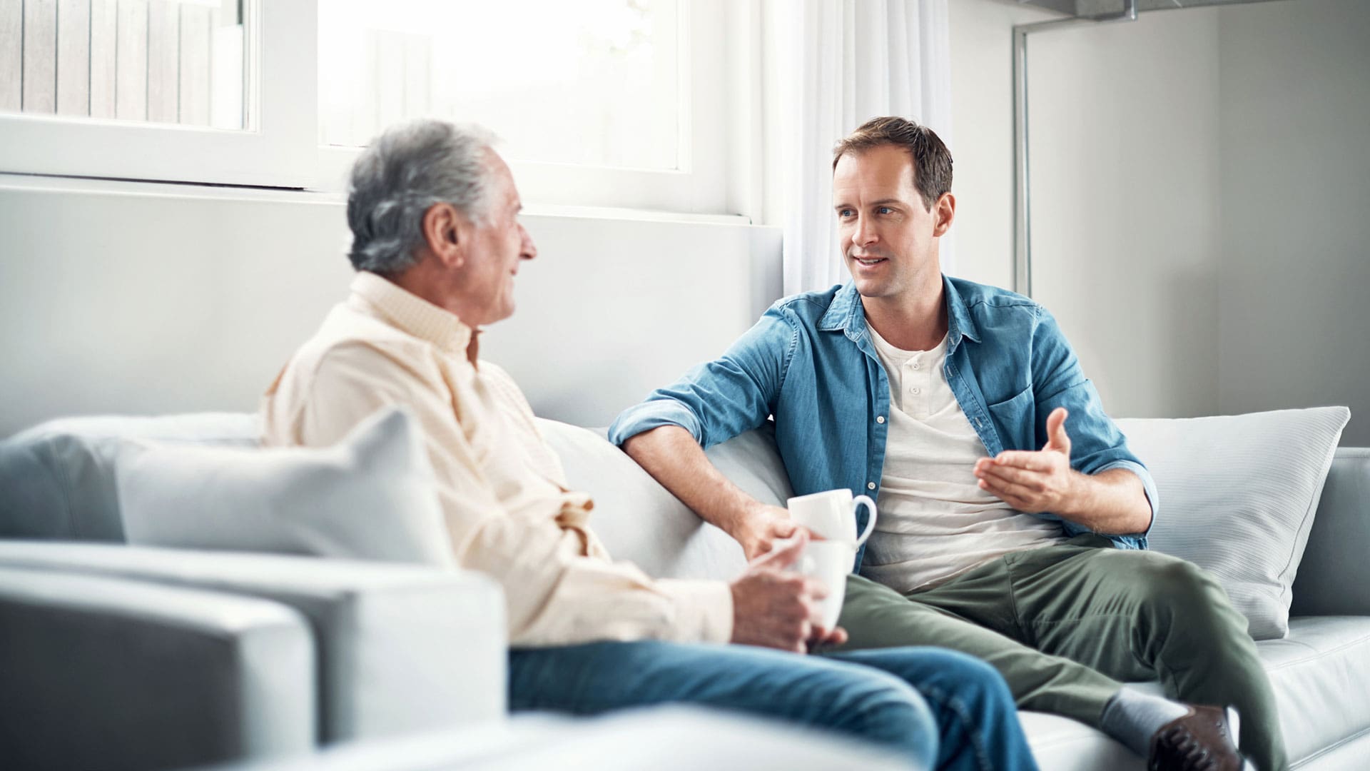 man talking with his senior father over coffee at home